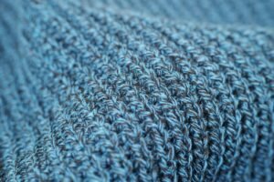 Macro shot of blue wool knit fabric showing intricate woven pattern and texture.